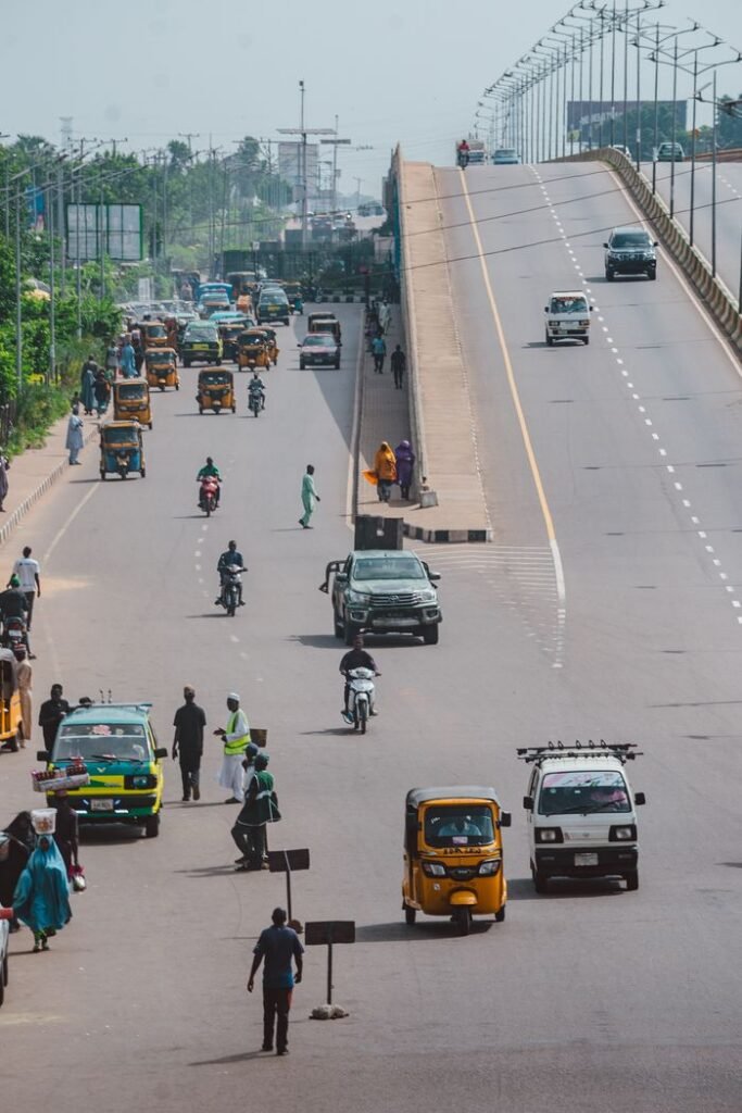 A busy urban road with vehicles and pedestrians under a clear sky, capturing everyday city life.